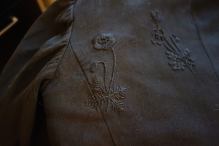 Two flowers embroidered with black floss on black gabardine